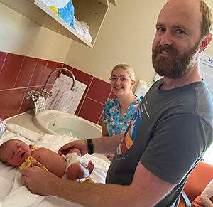 A female midwife watches a man care for a newborn baby.