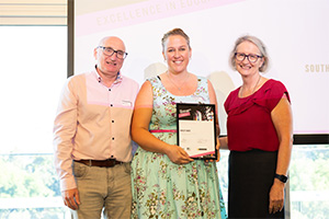 Hayley Jukes stands between a man and woman. She holds a WANMEA 2025 finalist certificate.