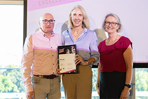 Nicole Slavin stands between a man and woman. She holds a WANMEA 2025 finalist certificate.
