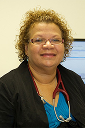 Stephanie Trust sits in front of a computer monitor. She wears a stethoscope around her neck.