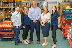 Five people stand surrounded by crates and boxes of food 