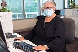 A woman wearing a surgical mask sits in front of the keyboard and computer.