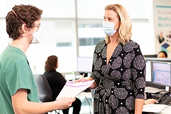 A man and woman wearing surgical mask talk in an office.