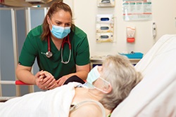 A female doctor holds the hand of an older woman in a hospital bed.