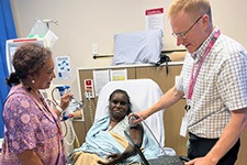 A female nurse (left) and a male doctor (right) treat the left arm of an Aboriginal women (centre) sitting in a hospital bed.