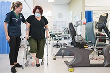 A female health professional stands beside a woman who is walking using elbow crutches