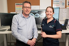 A male and female health professional stand in front of a computer monitor which displays a medical image.