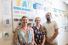 Three health professionals stand in front of a number of colourful posters on a display board