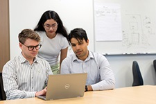 Three people review data on a laptop computer