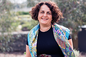 Dr Daniela Vecchio stands in a garden setting. She is wearing a colourful scarf across her shoulders