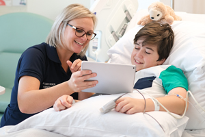 allied health professional holding iPad interacting with paediatric patient in hospital bed