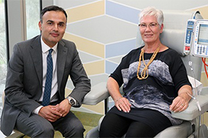 A man sits next to an older woman who is receiving immunotherapy treatment