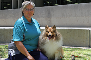 A woman sits beside a dog in a garden setting