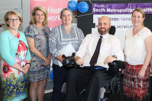 A man in a wheelchair and four women in front of display boards and banners