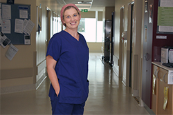 A woman wearing surgical scrubs stands in a hallway