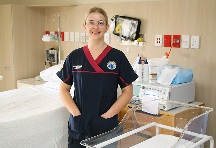 A female midwife stands between a bed and a newborn's cot