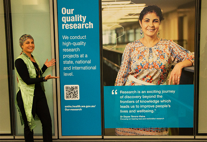 a woman stands beside two panels of artwork about research