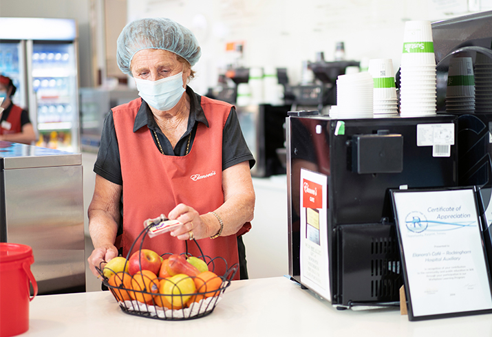 A woman stands in a kitchen environment and places fruit into a fruit bowl.