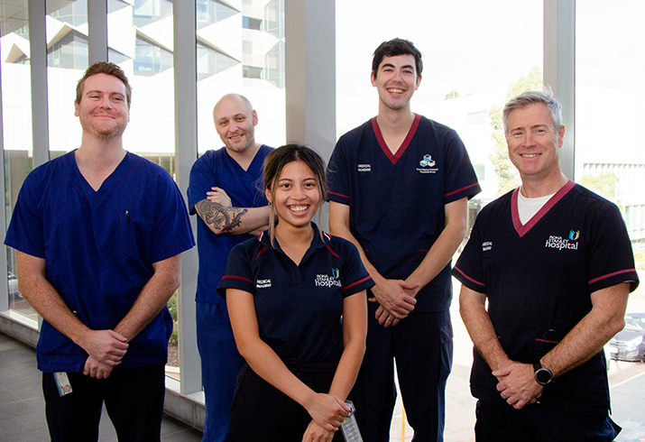 A group of five health professionals stand in front of a window