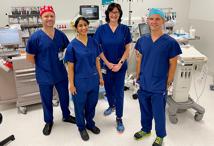 Two men and two women stand together smiling in hospital scrubs inside a theatre