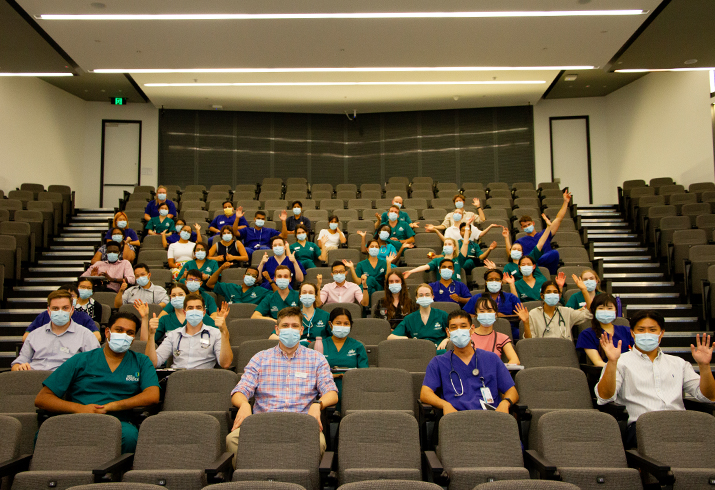 Men and women sit in an auditorium, physically distanced and wearing face masks.