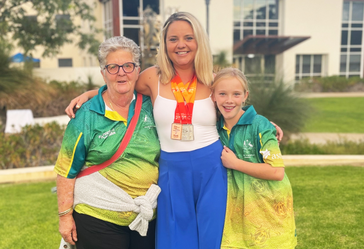 A woman wearing multiple winners medals stand between an older woman and a teenage girl in a garden setting