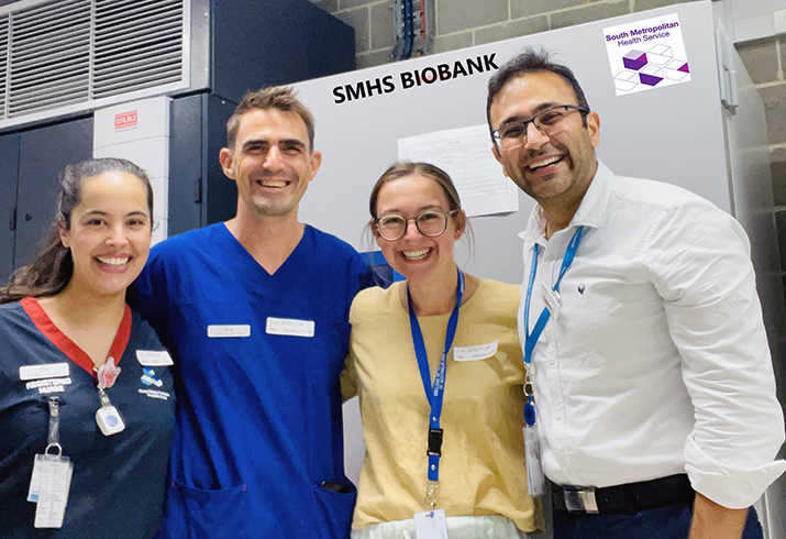 Two male and two female health professionals stand in front of a freezer.