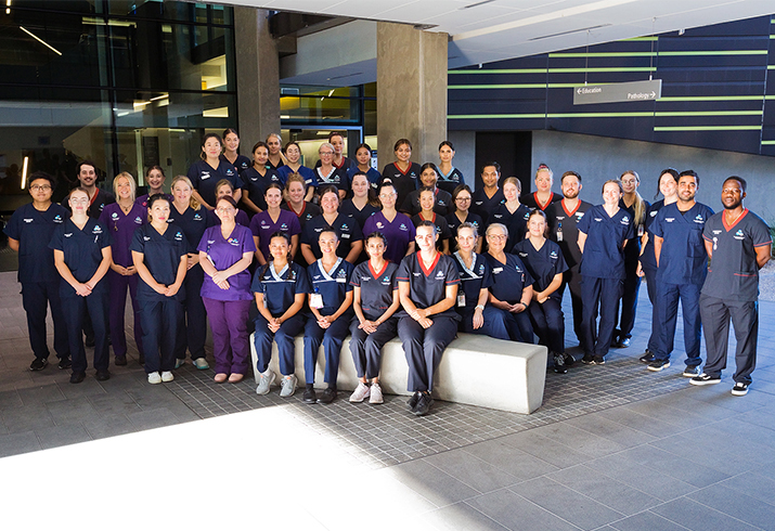 A large group of 2023 nursing and midwifery graduates standing together outside a building