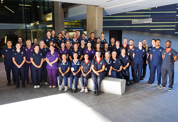 A large group of 2023 nursing and midwifery graduates standing together outside a building
