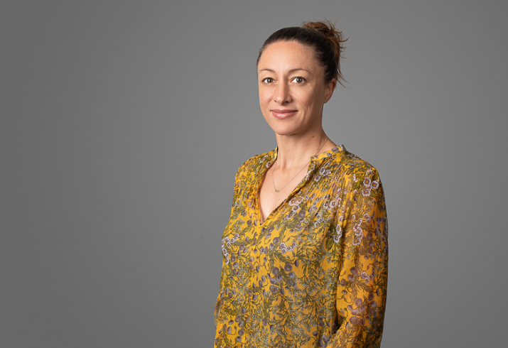 Fiona Stanley Fremantle Hospitals Group Endocrinologist Dr Ashley Makepeace standing in a grey room, wearing a yellow blouse and smiling at the camera.