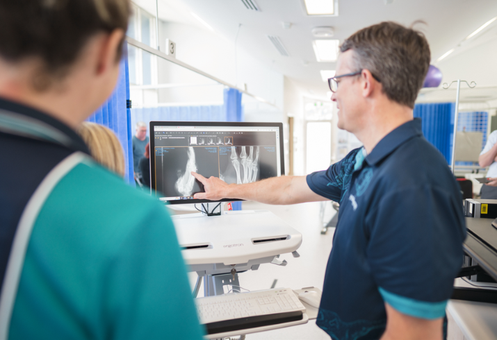 Man in blue pointing to work station on wheels, displaying a fracture.