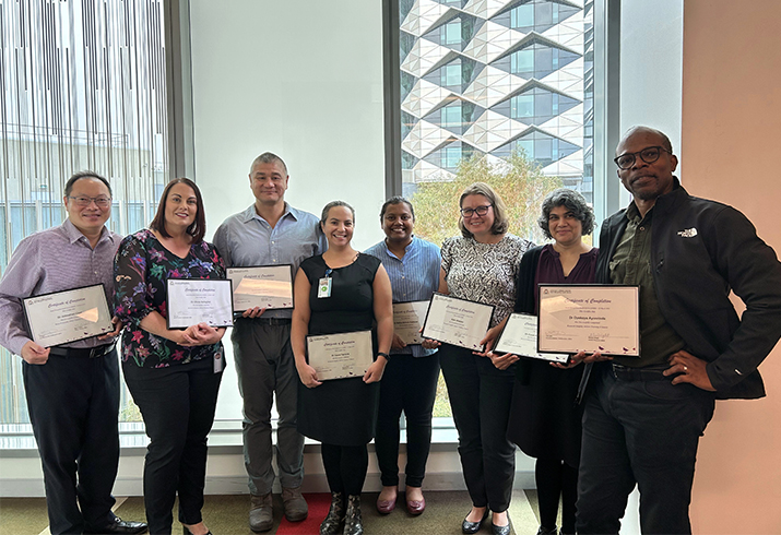 A group of eight SMHS Research Integrity Advisors stand together holding framed certificates