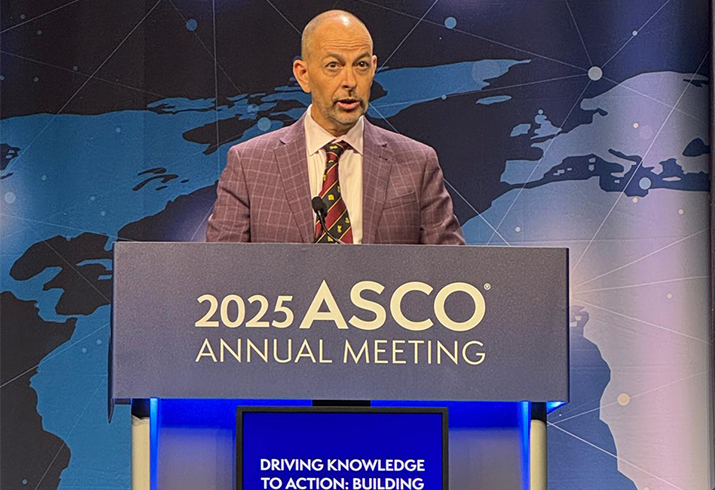 Professor Dickon Hayne stands behind a podium. A sign on the podium reads 2025 ASCO Annual Meeting